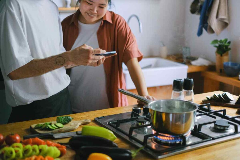 Twee mensen koken samen in een keuken met groente en een pan op het fornuis.
